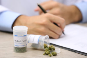 doctor writing prescriptions near bottle of medical cannabis