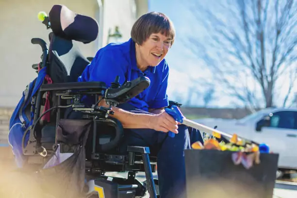 woman in blue with ms outside in wheelchair watering potted flowers
