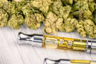 THC extractor de aceite de vape pluma cerca con hoja de marihuana en la mesa de madera blanca