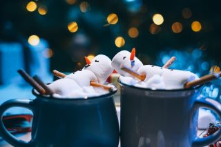 a mug with hot chocolate on a wooden table with a marshmallow man who is resting in a mug